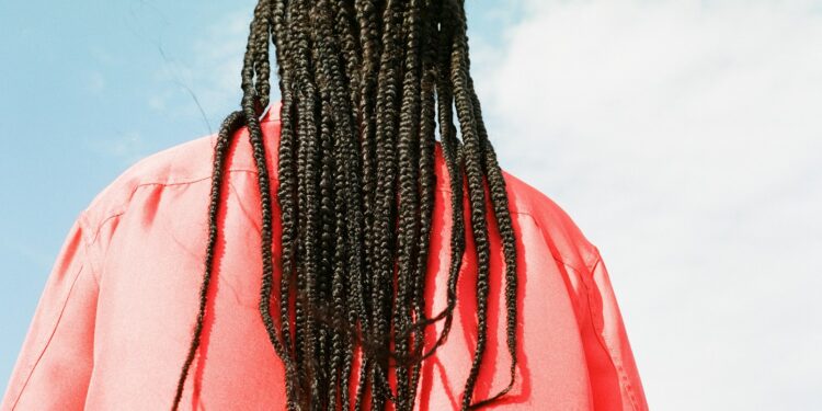 a man with long dreadlocks standing in front of a blue sky